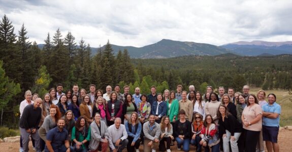 Large group of people pose for a photo, with a mountain in the distance